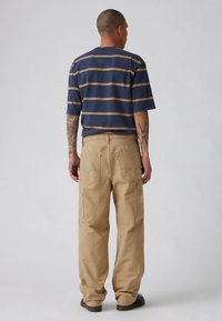 Καθημερινό μπλουζάκι με ρίγες σε ναυτικό μπλε με χρυσές γραμμές, σε συνδυασμό με άνετο μπεζ παντελόνι με πλαϊνές τσέπες και λογότυπο στο πίσω μέρος.