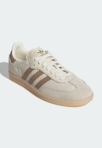 Sneakers Adidas montantes en beige et marron clair avec un dessus en tricot texturé, un embout en daim, une semelle en caoutchouc et une languette avec logo.