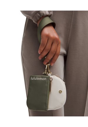 Pungul Lululemon verde și alb, cu două compartimente cu fermoar, accente de hardware aurie și un mâner texturat. Design compact și funcțional.