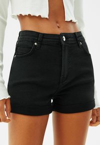Svarta jeansshorts med hög midja och uppvikta fållar, med två framfickor och gylf med dragkedja samt en knappstängning, slät textur.