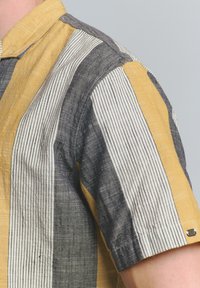 Korte mouwen shirt van gestreept fabric met gele, grijze en witte kleuren. Gevoerd, met een kraag en een klein metalen accent op de mouw.