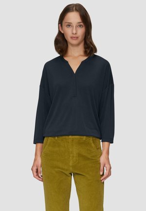 Navy losvallend shirt met een V-hals en driekwart mouwen, gecombineerd met olijfgroene corduroy broek met zijzakken en een gestructureerde stof.