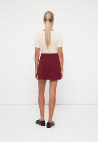 Crème kleurig top met korte mouwen gecombineerd met een bordeauxrode minirok. Eenvoudig ontwerp met een gladde textuur. Zwarte platte schoenen maken de look compleet.