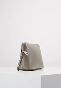 Borsa a tracolla in pelle grigia con una texture liscia, chiusura con zip e una tracolla in catena argentata. Presenta un logo del brand discreto sul davanti.