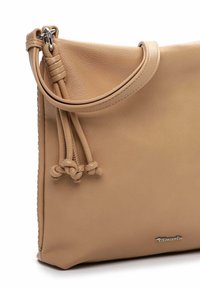 Beżowa skórzana torebka o gładkiej fakturze, ozdobiona supełkowanym sznurkiem i srebrną metką z logo. Kompaktowy, prostokątny kształt.