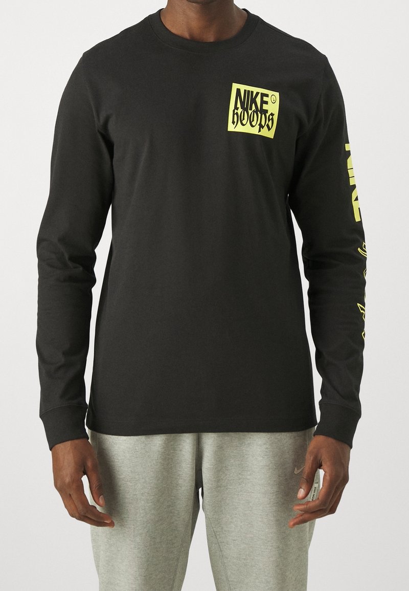 T-shirt a maniche lunghe nera in cotone, con una grafica gialla "NIKE HOOPS" sul petto e lettering giallo lungo la manica sinistra.