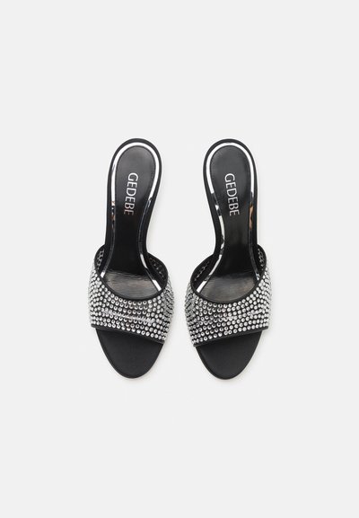 Black open-toe sandals with a wide rhinestone-embellished strap, glossy finish, and a smooth, flat sole. Brand name inside: Gedebe.