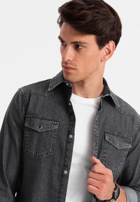 Grijze denim shirt met twee borstzakken, drukknoopsluitingen, en een contrasterend wit onderhemd, met een klassieke kraag en een gestructureerde stof.