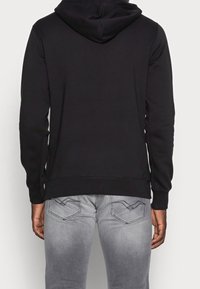 Sudadera negra con capucha y mangas largas, fabricada en un material suave. Presenta un dobladillo acanalado, textura suave y un diseño sencillo. Se lleva con jeans gris claro.