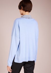 Ljusblå tröja med avslappnad passform, långa ärmar och ribbat nederkant. Bärs över en randig skjorta med krage. Har en mjuk textur.