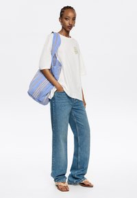 Camiseta de algodón blanca con estampado floral verde, bolsa de mano a rayas azules, jeans de pierna ancha de color azul claro y sandalias beige con bordes rizados.