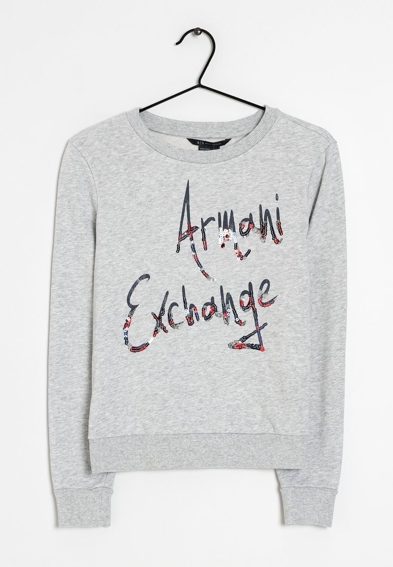 Sweat-shirt gris clair à manches longues avec poignets et ourlet côtelés, présentant le texte "Armani Exchange" orné de paillettes multicolores sur le devant.