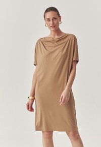 Cowl-neck, lyhythihainen mekko, joka on valmistettu sileästä, vaaleasta kankaasta. Polvipituinen, rento istuvuus, jossa on hienovarainen kiilto ja sivuhalkiot.