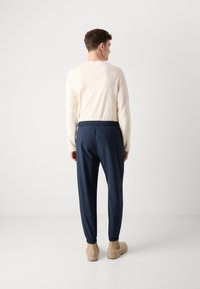 Marine joggerpants met elastische tailleband, gecombineerd met een crèmekleurige trui, gedragen met tan enkellaarzen. Glad materiaal en aansluitende manchetten zichtbaar.