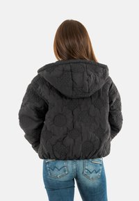 Zwarte gewatteerde jas met een capuchon, voorzien van gestructureerde patronen en een ronde silhouet, gecombineerd met blauwe spijkerbroeken.