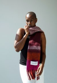 Wollen sjaal met horizontale gradient strepen in rijke rode en paarse tinten, met franjes aan de uiteinden en een zichtbare witte label met de tekst "ARCTIC FOX."