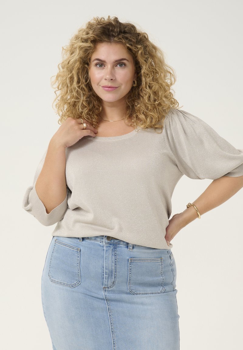 Lichtbeige, glanzende pullovertrui met pofmouwen. Gecombineerd met een lichtblauwe denimrok met achterzakken. Soepele textuur.