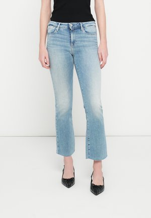 Ανοιχτό μπλε τζιν παντελόνι με ελαφρώς καμπυλωτή γραμμή, πέντε τσέπες και ξεφτισμένες άκρες. Συνδυασμένο με μαύρες γόβες με μυτερό άκρο.