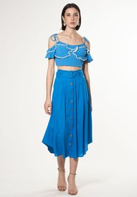 Completo blu in due pezzi con un crop top a volant con spalline sottili e una gonna alta in vita con bottoni sul davanti e una cintura.
