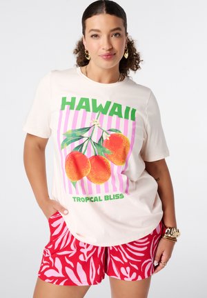 Vrouw met krullend haar die een wit "Hawaii Tropical Bliss" T-shirt met oranje fruitafbeelding en rode korte broek met patroon draagt, staand met hand in zak.