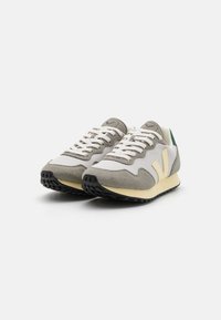 Sneaker con una tomaia in rete grigia, dettagli in suede, lacci bianchi e una suola intermedia gialla. Presenta una suola in gomma nera e un tab sul tallone verde.