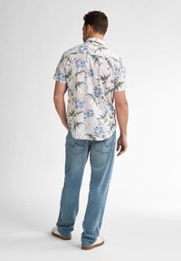 Camisa de flores de manga corta, de color claro, con flores azules y hojas verdes, combinada con pantalones vaqueros holgados y zapatillas blancas.