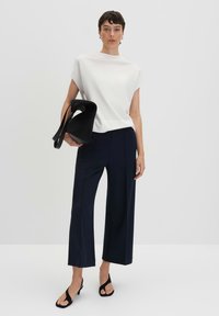 Haut blanc à manches courtes, pantalon large bleu marine, sac noir à finition texturée et sandales à talons hauts noires. Design simple et moderne.