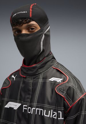 Sort racingdragt med røde accenter og hvidt Formel 1-logo. Materialet har et quiltet mønster, høj krave og integreret ansigtsmaske.