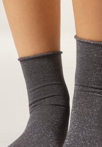 Grå ankelsockor av glansigt, strukturerat tyg, med en mjuk mudd och en lätt glittrande yta som reflekterar ljus.