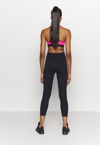 Soutien-gorge de sport rose et noir, leggings noirs taille haute, tous deux en matière extensible ; la vue de dos met en valeur le design ajusté et les textures lisses.