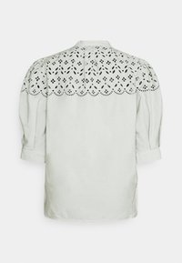 Blouse blanche à manches trois-quarts, dotée d'un empiècement en broderie anglaise et de bords festonnés sur le haut du dos et les épaules.