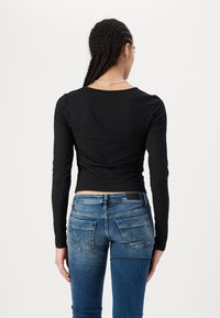 Svart langermet cropped topp laget av glatt stoff, kombinert med tettsittende blå denimjeans med baklommer og lette slitasjer.