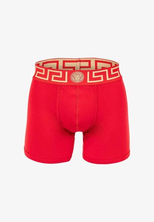 Red boxer shorts featuring a golden patterned waistband with a lion emblem. Soft material, snug fit, and mid-thigh length.
