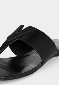 Μαύρο δερμάτινο σανδάλι slide με φαρδιά λουράκι και V-σχήματος λεπτομέρεια πάνω από το κουντεπιέ, ανοιχτό δάχτυλο και επίπεδη σόλα.