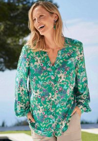 Groene bloemenblouse met een knoopsluiting, lange mouwen en een losse pasvorm. Heeft paarse en blauwe accenten in het stofpatroon.
