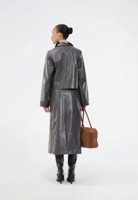 Veste en cuir gris avec une longue jupe assortie, dotée d'un col, d'une texture lisse et d'un sac à main beige. Design élégant et moderne.