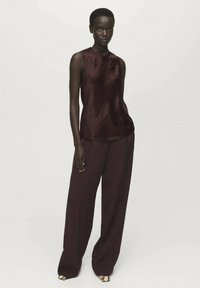 Top bordeaux senza maniche con una finitura texturizzata, abbinato a pantaloni a gamba larga dello stesso colore, caratterizzati da un design morbido e fluido.