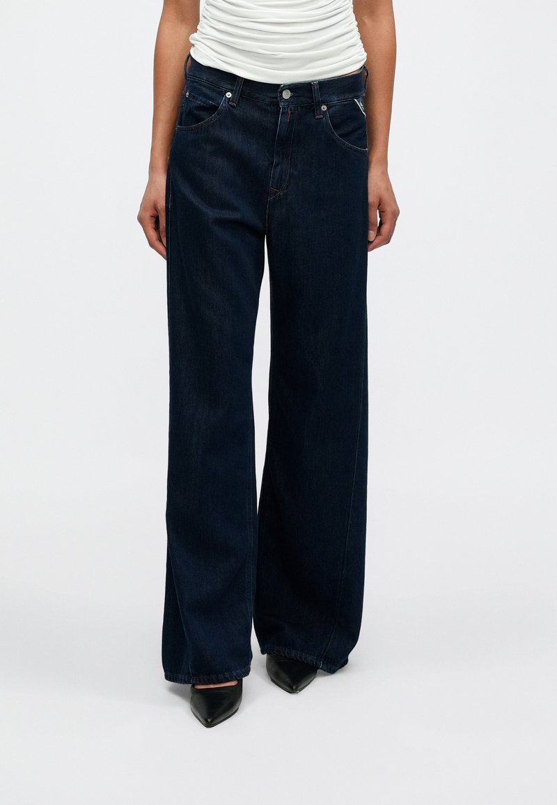 Τζιν παντελόνια με φαρδιά μπάτα, σκούρου χρώματος τζιν ύφασμα, ψηλή μέση, δύο εμπρόσθιες τσέπες και λεπτομέρειες σε αντίθετη ραφή. Το ύφασμα έχει λεία υφή.