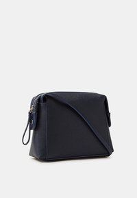 Borsa a tracolla in blu navy con texture, dotata di tracolla regolabile e chiusura superiore con zip, mostrata su uno sfondo grigio chiaro uniforme.