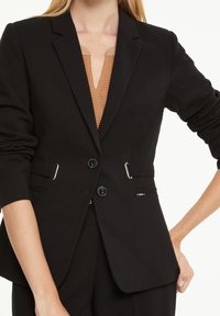 Černý přizpůsobený blazer, jednobarevný, má dva knoflíky, boční kapsy s kovovými akcenty, slim fit a strukturované ramena.