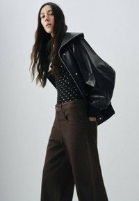 Veste oversize en cuir noir, body à pois et pantalon large marron, avec une coupe classique et une coupe structurée.