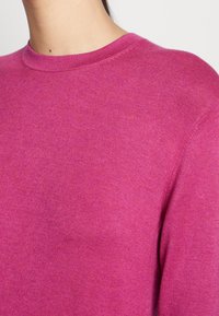 Fuchsiový svetr s kulatým výstřihem, vyrobený z jemného pleteného materiálu. Vyznačuje se hladkým povrchem a mírným strečem.