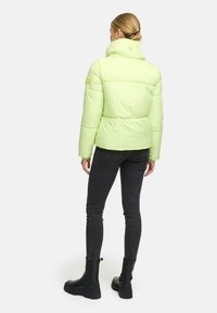 Limoengroene donsjack met een hoge kraag, een gladde textuur en gestikte panelen, gecombineerd met zwarte slim-fit jeans en enkellaarsjes.