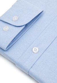 Jasnoniebieska koszula z długim rękawem starannie złożona, z widocznym zapiętym mankietem i przednią plisą z białymi guzikami oraz drobną fakturą tkaniny.