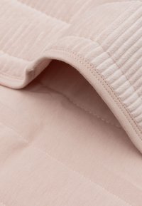 Tissu matelassé rose clair avec une texture douce, présentant des accents nervurés et un revers lisse, partiellement replié pour montrer les couches.