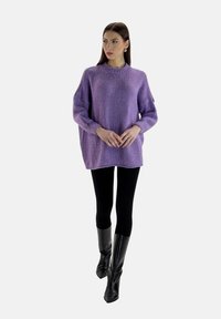 Fioletowy sweter robiony na drutach z okrągłym dekoltem, luźny krój i długie rękawy. Połączony z czarnymi legginsami i błyszczącymi, wysokimi botkami.