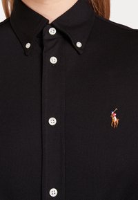 Chemise noire boutonnée avec un col boutonné et un petit logo brodé d'un joueur de polo sur la poitrine.