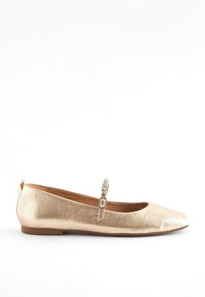 Chaussure plate métallique dorée avec une petite bride à boucle scintillante sur le dessus et un bout arrondi sur fond blanc.