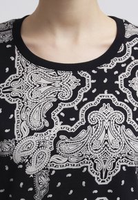 Svart tröja med vitt paisleymönster, med ribbad krage och intrikata mönster. Mjuk textur med en detaljerad design genom hela plagget.