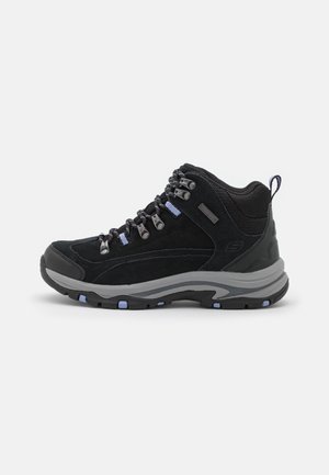 Botte de randonnée noire et grise avec cheville rembourrée, œillets métalliques, accents de lacets bleus et semelle texturée sur fond blanc.